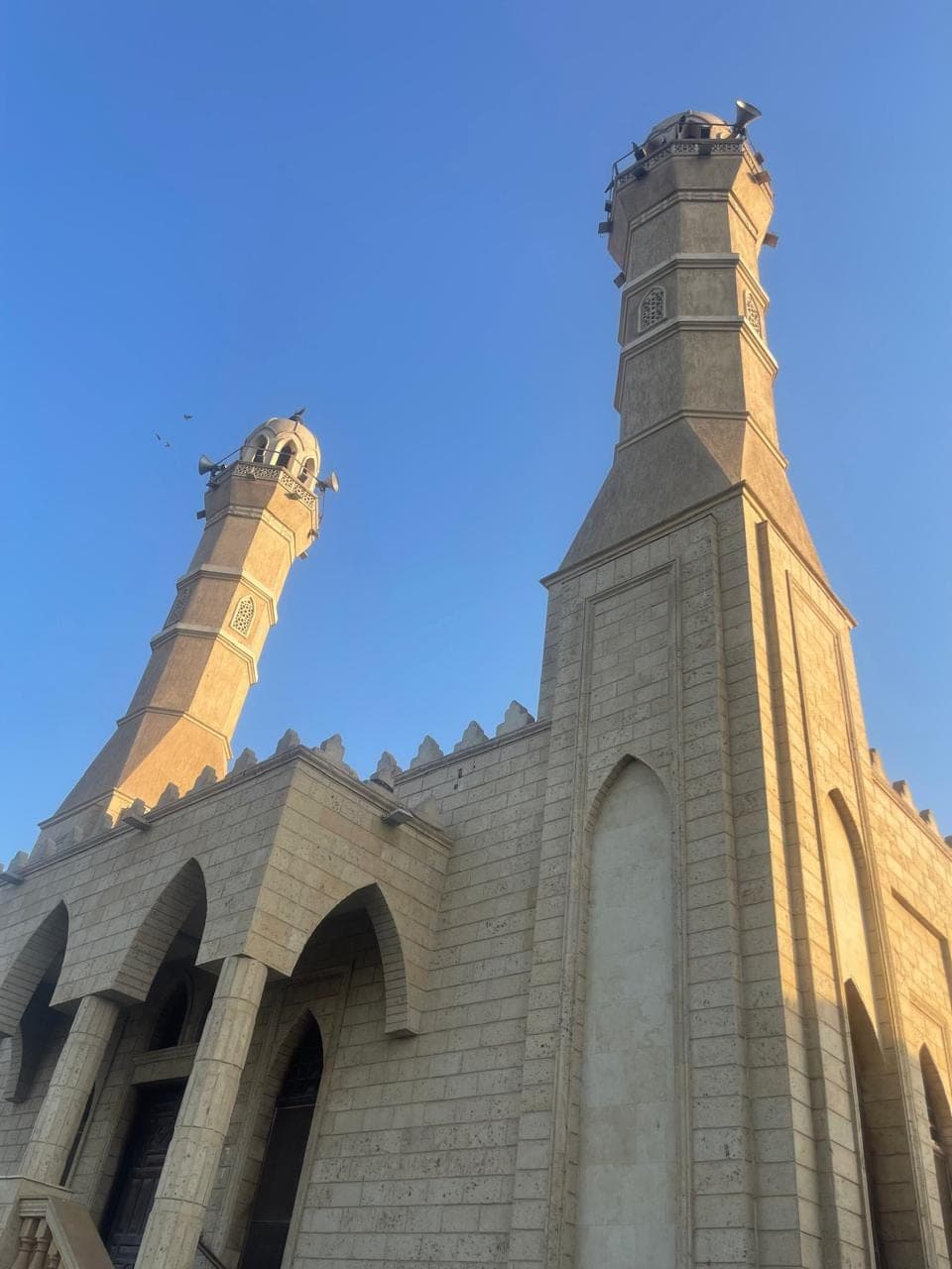 Almaghfera Masjid — the stone minarets seen from the corner against a clear sky