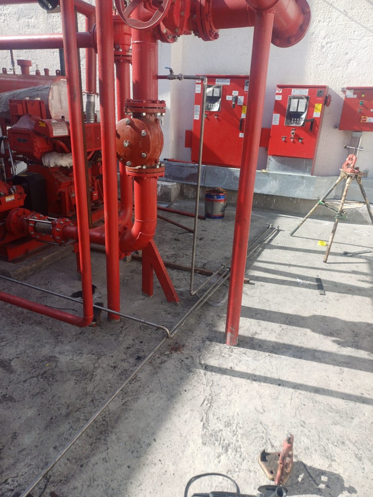 A red diesel-driven fire pump and its flanged suction pipework, with three red fire-pump controller cabinets on the wall beside it
