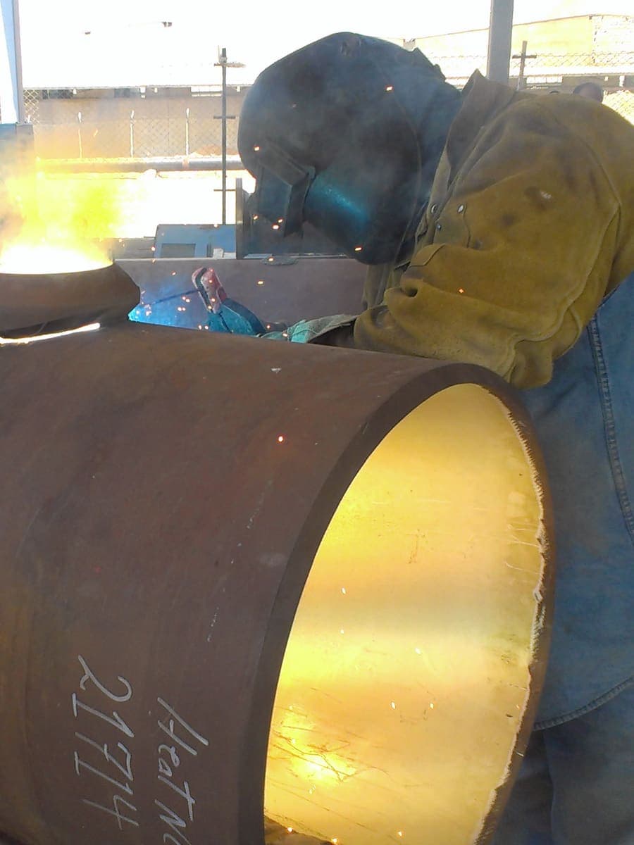 Welders joining a large-diameter hydrant pipe section at Cairo Airport Terminal 2, the bore glowing from the weld