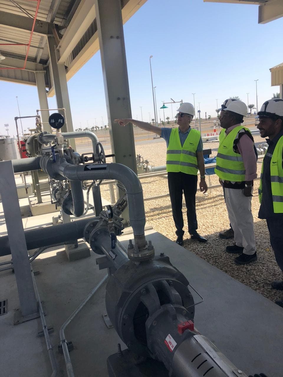 Engineers in high-visibility vests reviewing pump and valve pipework at a commissioned fuel installation