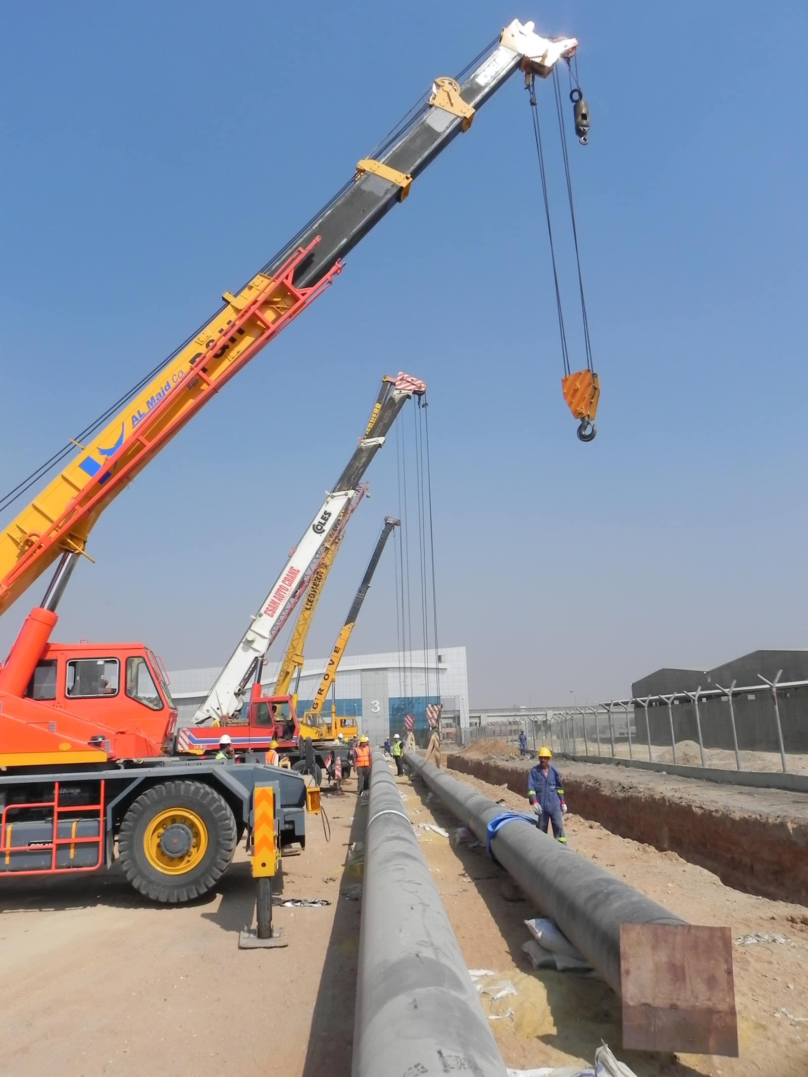 Mobile cranes lowering a coated hydrant main into the trench at Cairo Airport Terminal 2